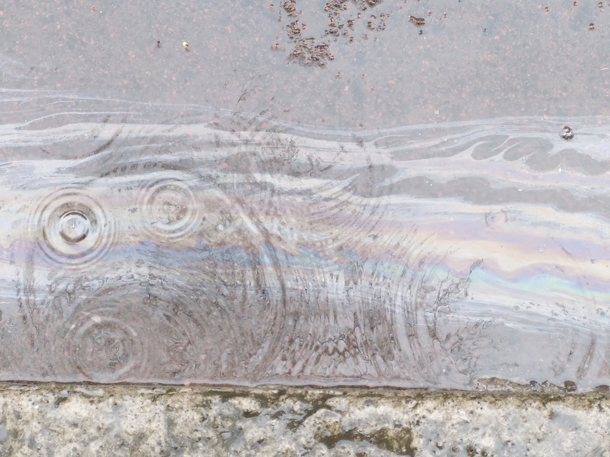 Raindrops landing in an oil puddle